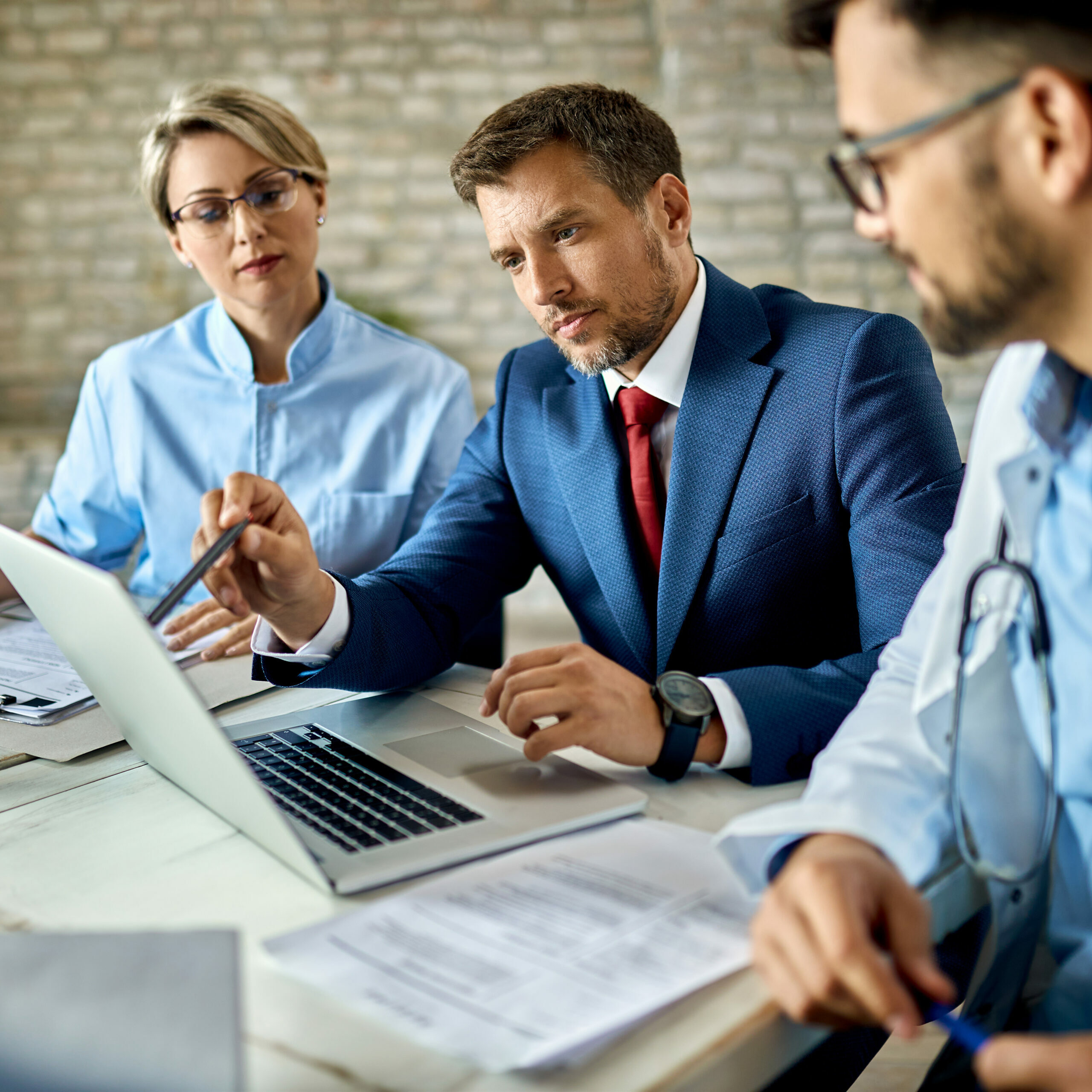 Mid,Adult,Businessman,And,Group,Of,Doctors,Working,On,A Mid adult businessman and group of doctors working on a computer during a meeting.